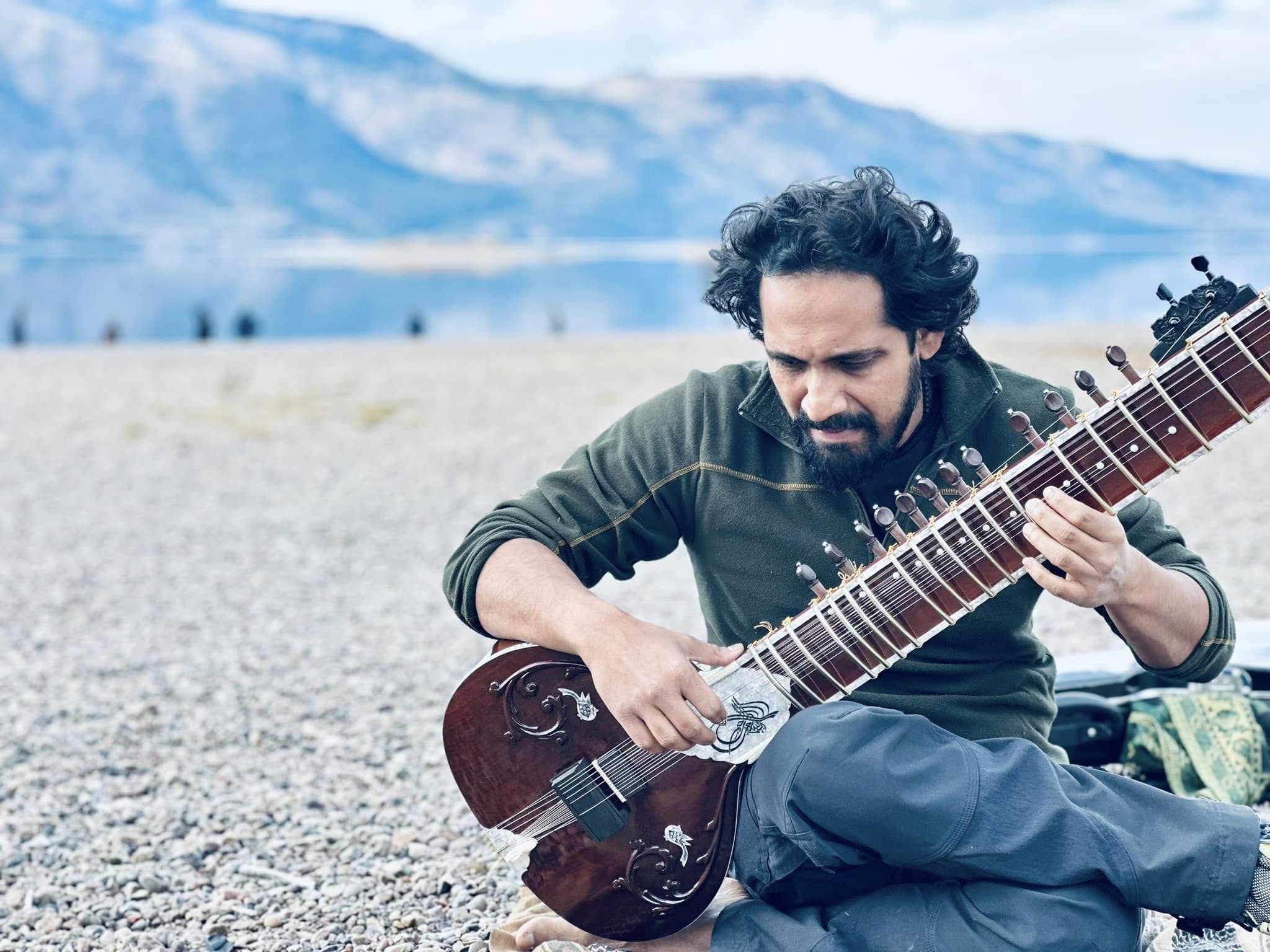 Playing sitar outdoors by mountains and lake